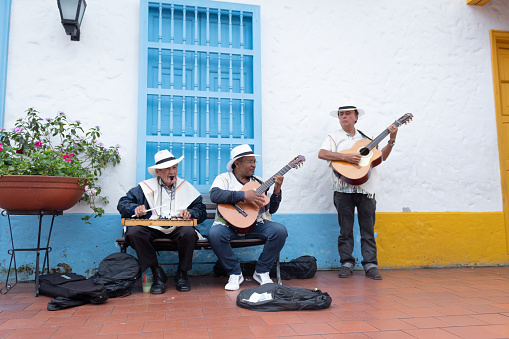 Medellin, Colombia - July 30, 2022: Three senior musicians of traditional Colombian music, two of them playing a guitar and the other a xylophone . They are all outside a house.