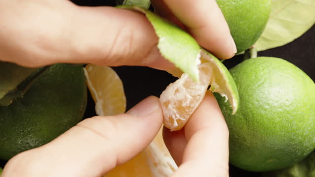 I peel a tangerine with a green peel, and the camera passes by. View from above. slow motion