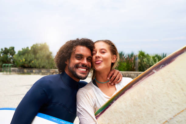 headshot portrait multi racial heterosexual couple in love happy smiling surfers with surfboards - human face heterosexual couple women men imagens e fotografias de stock