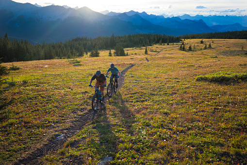 Two men go for a mountain bike ride in the Rocky Mountains of Canada. They are riding enduro-style mountain bikes and wear cycling helmets.