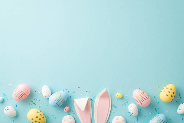 easter concept. top view photo of easter bunny ears colorful eggs and sprinkles on isolated light blue background with copyspace - pasen stockfoto's en -beelden