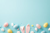 Easter concept. Top view photo of easter bunny ears colorful eggs and sprinkles on isolated light blue background with copyspace