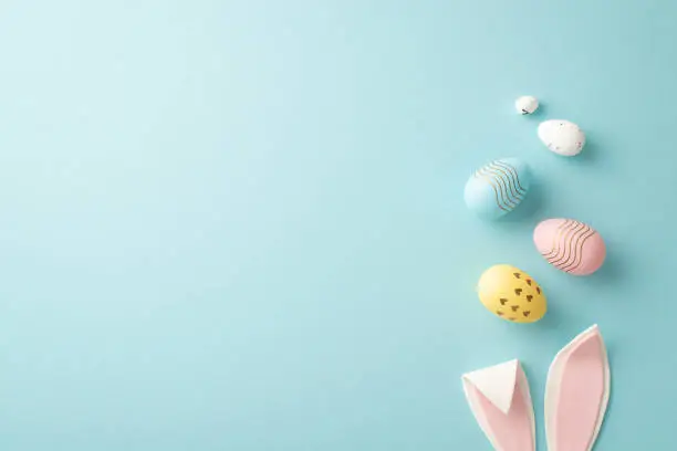 Photo of Easter concept. Top view photo of easter bunny ears and colorful eggs on isolated pastel blue background with copyspace