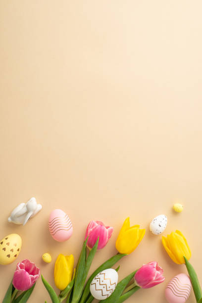 istock Easter decor concept. Top view vertical photo of colorful easter eggs ceramic easter bunny and tulips on isolated light beige background with blank space 1467968853