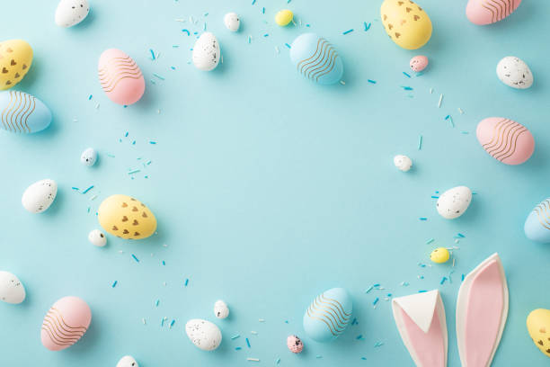 istock Easter composition concept. Top view photo of yellow white blue pink eggs easter bunny ears and sprinkles on isolated pastel blue background with copyspace in the middle 1467969001