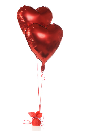 Two red, heart-shapped, helium-filled ballons anchored with red ribbons.  Isolated on white.