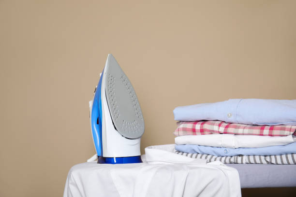 istock Modern iron, clean shirt and folded clothes on board against beige background 1467970912