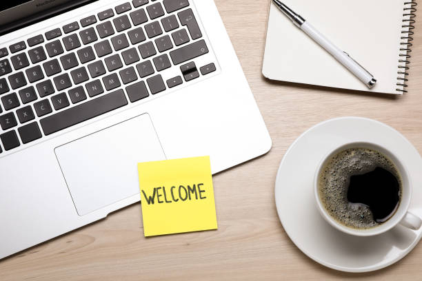 istock Paper note with word Welcome, laptop, coffee and notebook on wooden table, flat lay 1467971044