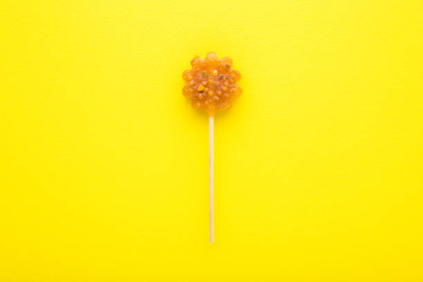 istock Honey candy on stick on bright yellow table background. Closeup. Sweet snack. Top down view. 1467971872