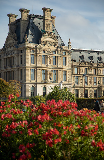 View of Pavillon de Marsan, Jardin des Tuileries and Louvre palace museum with red flowers in park on sunny day in Paris, France