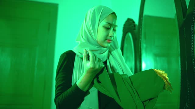 a Muslim woman takes and holds a mysterious green cloth in a green room which is very scary