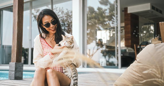 Happy young adult Asian woman hug and enjoy petting her cat at home balcony. Pet lover people concept