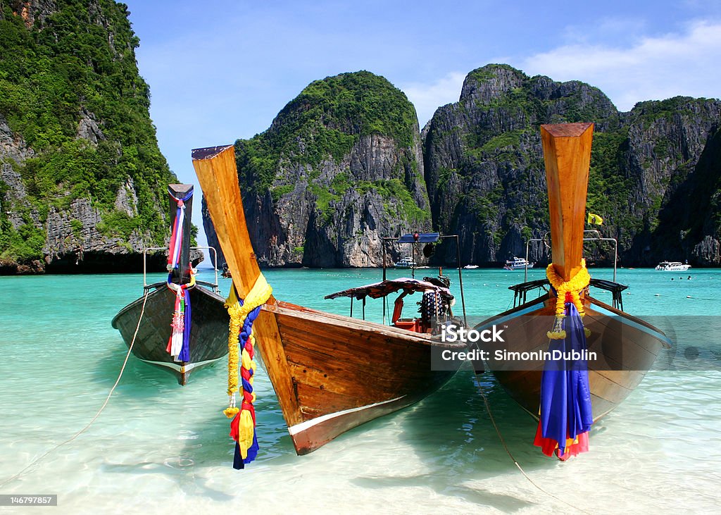 Long Boats, The Beach, Phuket, Thailand Long Boats anchored on Phi Phi Le Island, Phuket, Thailand. Bay of Water Stock Photo