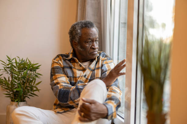 jubilado anciano en casa triste mira por la ventana serio - soledad fotografías e imágenes de stock