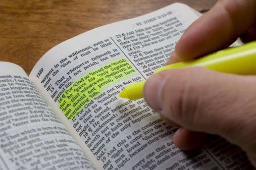 A man uses a highlighter to mark a bible verse, John 3:16.