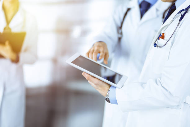 istock Group of unknown doctors use a computer tablet to check up some medical names records, while standing in a sunny hospital office. Physicians ready to examine and help patients. Medical help 1467988323