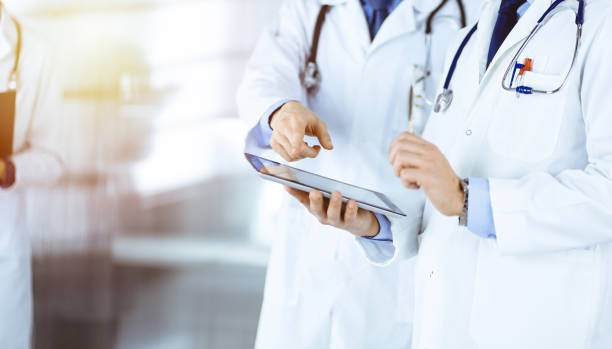 istock Group of unknown doctors use a computer tablet to check up some medical names records, while standing in a sunny hospital office. Physicians ready to examine and help patients. Medical help 1467988353