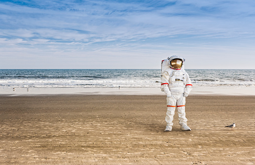 Space astronaut in a suit standing alone on the sandy beach by the ocean