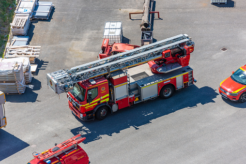 Full length side view of early 30s woman in turnout gear and helmet scaling ladder on back of parked fire engine.