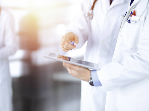 istock Group of unknown doctors use a computer tablet to check up some medical names records, while standing in a sunny hospital office. Physicians ready to examine and help patients. Medical help, insurance in health care 1467992232