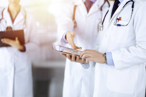 istock Group of unknown doctors use a computer tablet to check up some medical names records, while standing in a sunny hospital office. Physicians ready to examine and help patients. Medical help, insurance in health care 1467992249