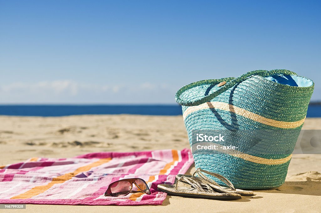 Relaxing at the beach Vibrant towel, beach bag and accessories spread out on the sand. Beach Towel Stock Photo