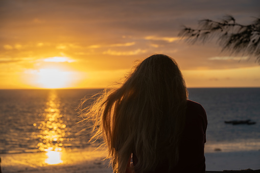 Young blonde girl from behind watching the sunrise on a beach in Zanzibar (Africa)