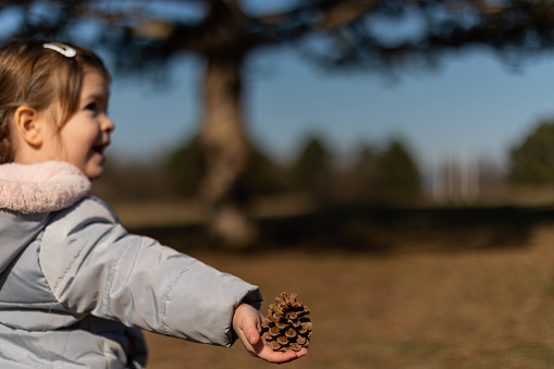 The girl is playing in the forest. She found a pine cone and enjoy playing with it. It's winter, but she's inhaling the fresh air, and enjoying the sunny day.