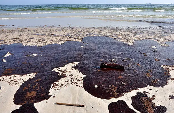 Oil spill on beach with off shore oil rig in background.
