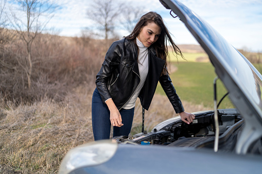 A young woman with a damaged car on the road uses the phone to consult a mechanic.