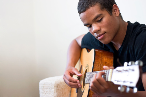 African American teen plays an acoustic guitar.