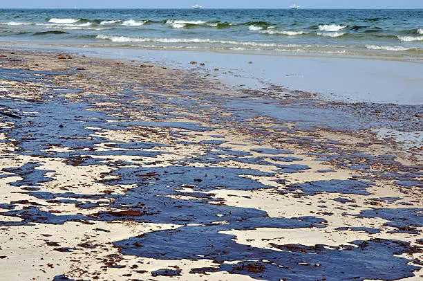 Oil spill on beach with oil skimmers in background.