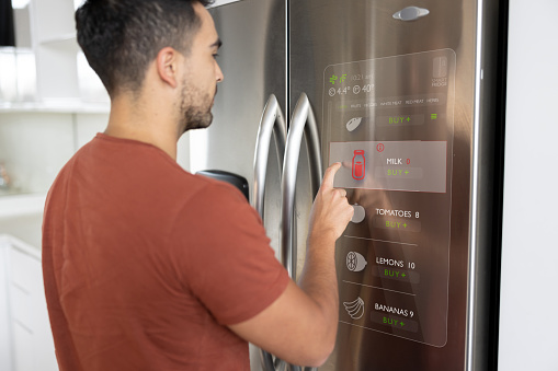Latin American man looking at the shopping list on the fridge at his smart home using an interactive screen - technology concepts