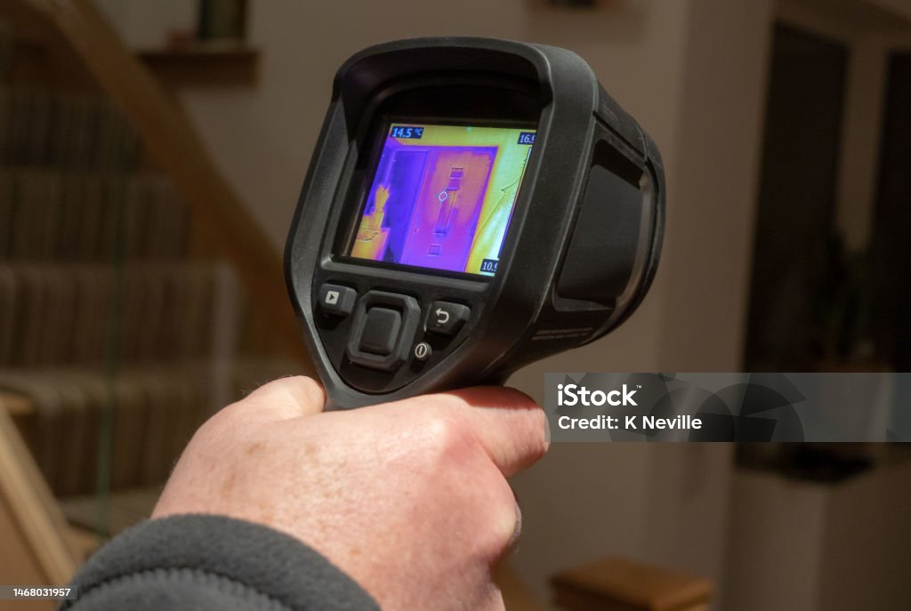 Handheld infrared thermal camera being used A male surveyor using a handheld infrared thermal camera, to inspect the interior of a domestic home, looking for heat anomalies. The camera viewfinder shows a coloured thermal image with varying temperature ranges. Examining Stock Photo