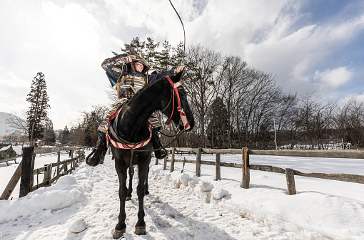 A retired old samurai warrior draws his bow taking aim from his horses back in the snow in rural Japan.