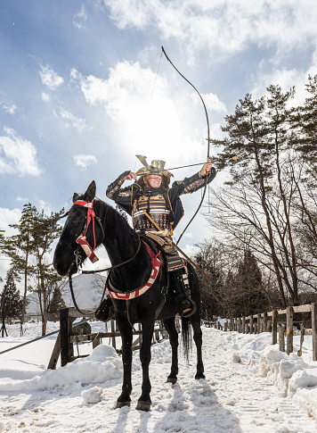 A retired old samurai warrior draws his bow taking aim from his horses back in the snow in rural Japan.