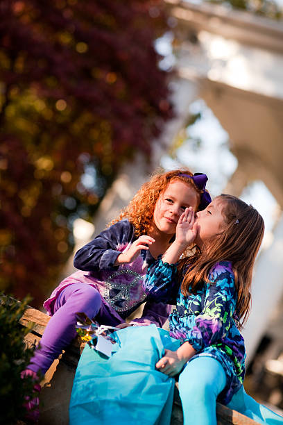 Two little girls telling secrets while one looks out stock photo