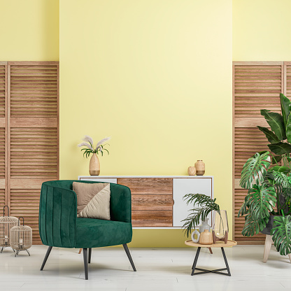 Cozy retro-chic interior with a green velvet armchair and a low white and hardwood cabinet in front of a vanilla yellow plaster wall background with copy space. A low coffee table with ceramic containers, vases on the white hardwood floor, birdcage lamps, and decoration (lush foliage: monstera, banana/palm tree, pillow) with 2 hardwood slat doors on each side. The 50s- 60s decoration, art deco style. A slight vintage effect was added. 3D rendered image.
