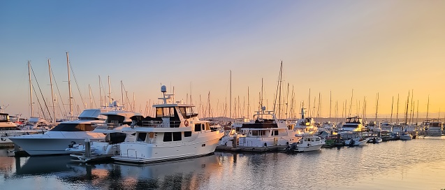 Luxury yachts at sunset. Marina of modern motor and sailing boats in sunshine. Reflection blue sky in water. Sea port dock. Travel and fashionable vacation.