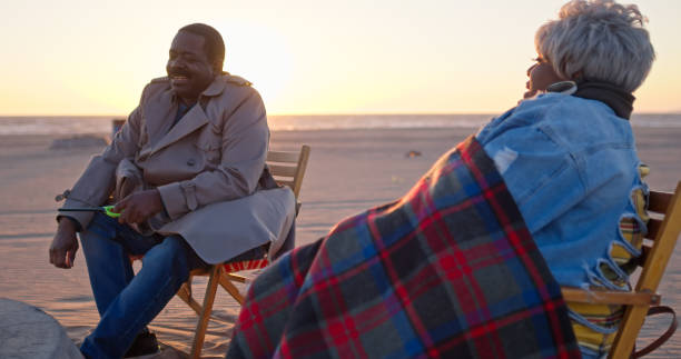 Senior African-American Couple Sit in Beach Chairs by Firepit at Sunset