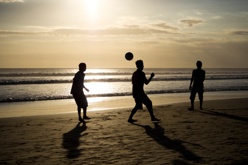 Three Kids are playing soccer on the beach in the sunset. The picture was taken on the Indonesian island Bali.