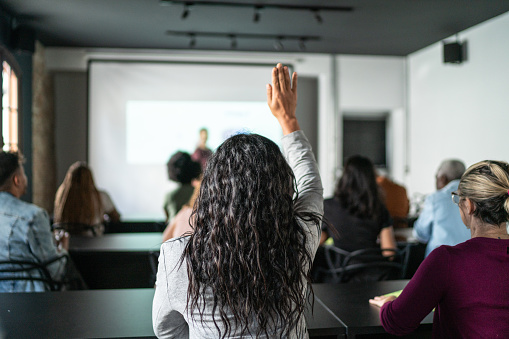 Woman with hand raised asking in the classroom or seminar