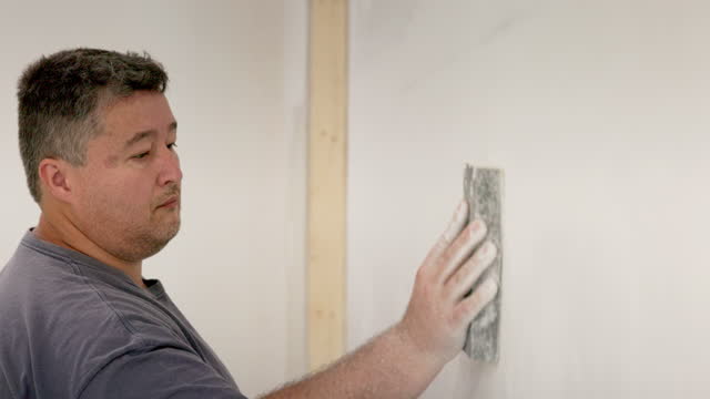 Caucasian handyman preparing the wall with sanding sponge.