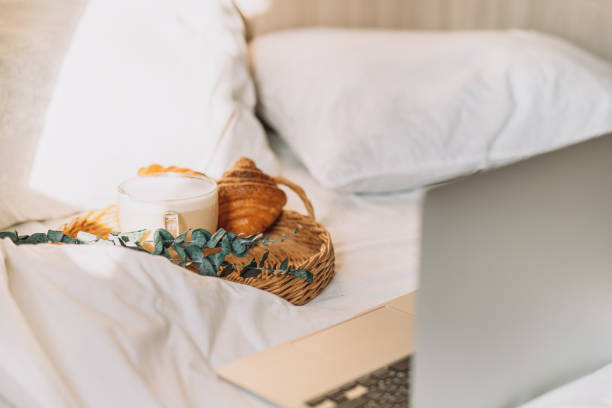 istock Wicker tray with croissants and coffee on white bed linen with laptop 1468069287