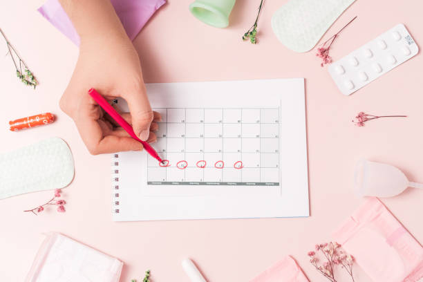 senhora marca com caneta vermelha de ponta de feltro no calendário o ciclo menstrual no fundo rosa com pílulas e guardanapo sanitário - tampon menstruation sanitary female - fotografias e filmes do acervo