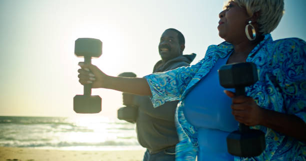istock African-American Senior Couple Lift Weights on the Beach While Backlit 1468073022
