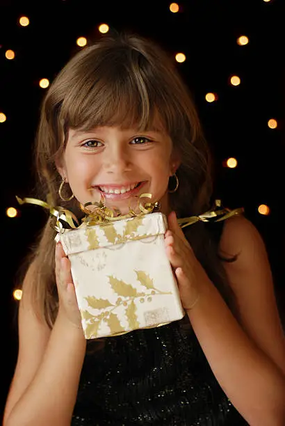 A cute young girl holding  a christmas gift, dark background with christmas light bokeh