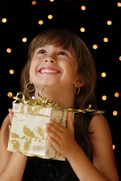 A cute young girl holding a christmas gift,dark background with christmas light bokeh