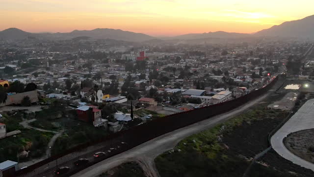 Time Lapse of the International Border Wall Between Tecate California and Tecate Mexico Near Tijuana Baja California Norte at Dusk Under Stunning Sunset with View of the City From the USA
