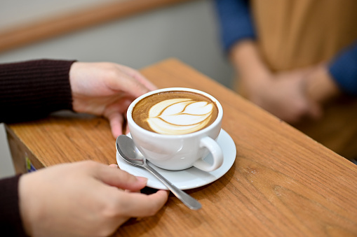 Close-up image of a female customer's hands holding a cup of latte, sipping coffee, relaxing in the coffee shop.